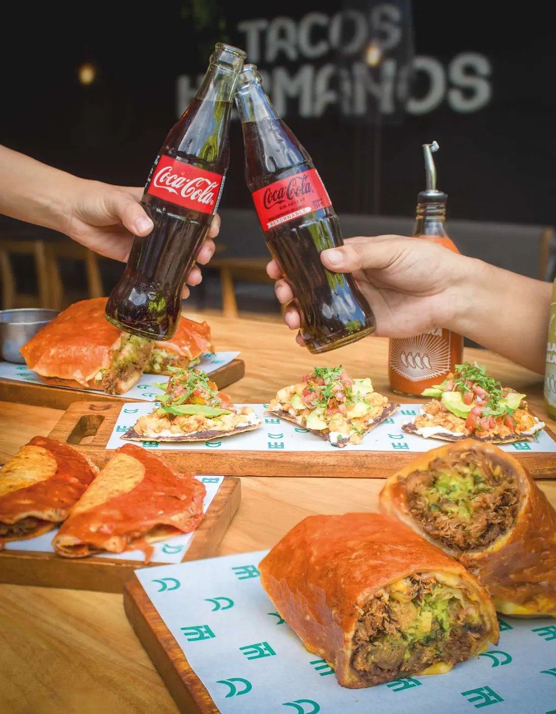 Brindis con Coca-Cola sobre una mesa llena en Tacos Hermanos